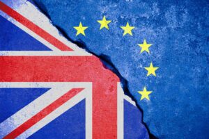 A cracked concrete surface displays the juxtaposition of the Union Jack flag on the left and the flag of the European Union with yellow stars on a blue background on the right, symbolizing the divide between the UK and the EU.