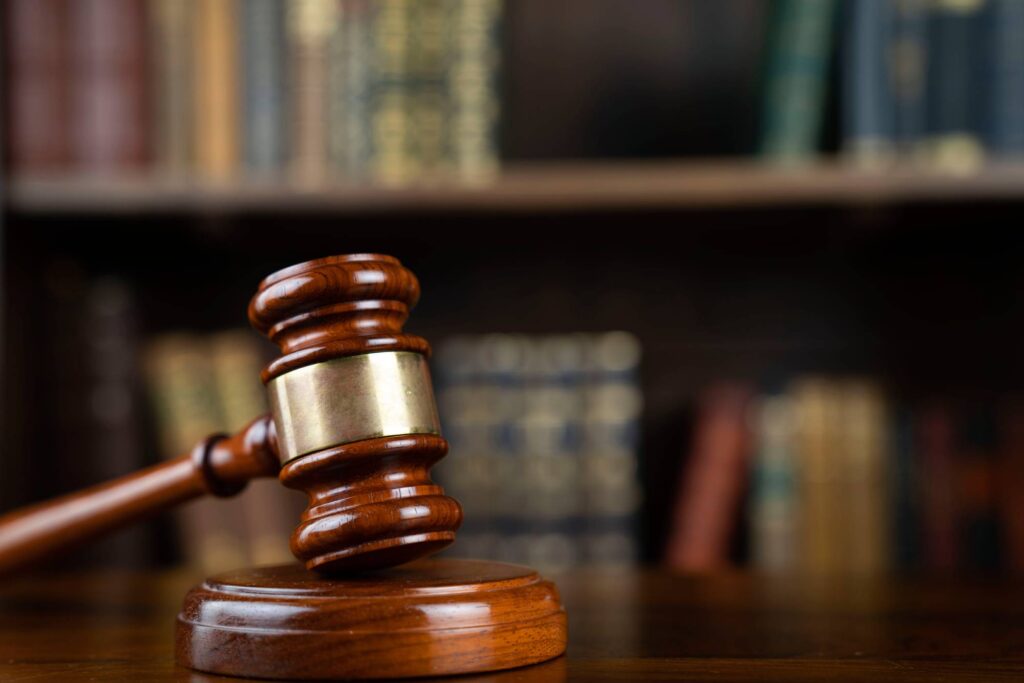 A wooden gavel rests on a sound block in front of a blurred background of books on a shelf, symbolizing law and justice.