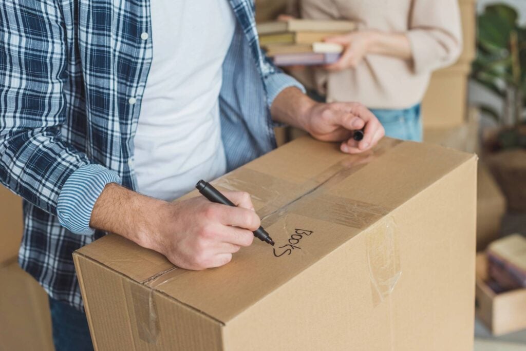 Man with moving box writing "books" on the top with a sharpie
