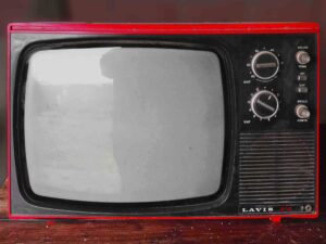 A vintage LAVIS 812 television with a red frame, black screen, and control knobs on the right side. The TV has dials for UHF and VHF channels, volume, tone, and brightness. The set is placed on a wooden surface against a blurred background.
