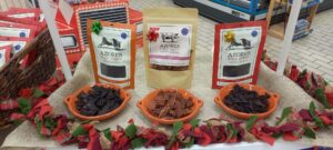 A display of beef jerky products labeled "Azores Beef Jerky," with one package of pork jerky in the center. Each packet is paired with a bowl of jerky pieces. The setup is decorated with a festive red and green plaid border on a burlap cloth.
