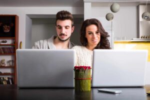 a couple both looking at their laptops and trying to make a decision