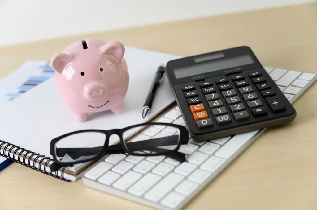 piggybank and calculator next to a notepad and keyboard