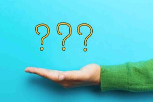 A hand in a green sweater is extended against a light blue background. Floating above the palm are three large, yellow question marks.