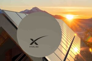 A circular Starlink satellite dish is mounted on the roof of a building with several solar panels. The sun is setting behind a mountain range in the background, casting a warm, golden light across the scene.