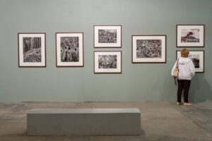 A person in a white hoodie views black-and-white art in a gallery, possibly exploring life and culture in Portugal; gray bench in front.