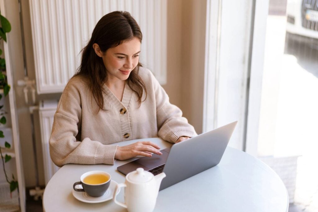 woman using her laptop at a table and drinking a tea
