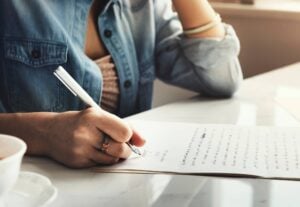 Person writing their notes by hand and drinking a cup of coffee