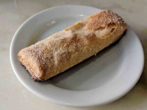 A sugared pastry on a white plate rests on a marble surface. The pastry has a golden-brown crust and is rectangular in shape, reminiscent of the delectable treats found in Portugal.